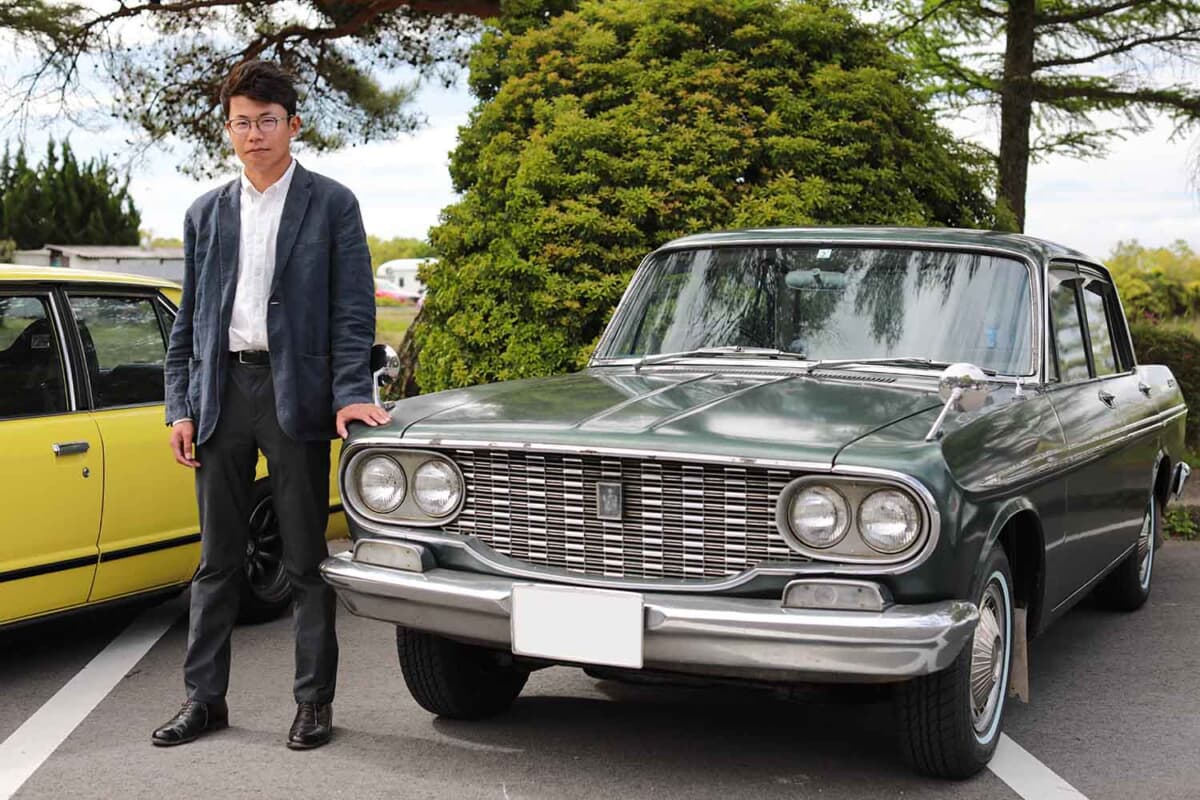 1964年式のトヨタ トヨペット クラウン デラックスとオーナーの西野さん。この日は愛車初お披露目のタイミングだったので、当時の若者のカジュアルフォーマルを意識したファッションで参加