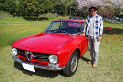 オーナーの“のり”さんと1971年式のアルファ ロメオ GT1300ジュニア。過去にフェラーリ F355やケータハムを所有していた“のり”さんは、現在はランドローバー ディフェンダー 110Tdi、ポルシェ 356レプリカ、トヨタ GRヤリス、フィアット 500D、ポルシェ カイエン ターボなども愛用