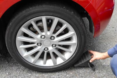 クルマが動かないようサイドブレーキを引き、交換するタイヤの対角線上にあるタイヤを輪止めで固定する