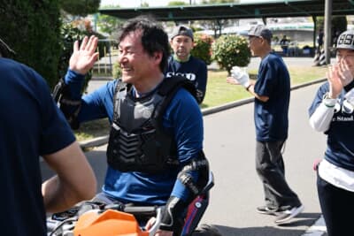 走行を終えヘルメットを脱いだ時に垣間見られる笑顔。そして周囲のボランティアスタッフの温かい拍手とハイタッチ。この場にいることの歓びである