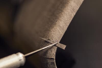 職人は、使用されているのと同一のベニアから色調を正確に合わせた微細な薄片をメスで切り出し、傷のある箇所に接着してホットプレートで密封する