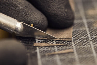 職人は使用されているのと同一のベニアから色調を正確に合わせた微細な薄片をメスで切り出し、傷のある箇所に接着してホットプレートで密封する