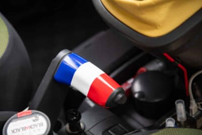 ルノー カングー：パーキングブレーキレバーは、不思議な形をしているのも2代目カングーの特徴。ここも味気ないプラスチック製なので、トリコロール柄でワンポイントアクセントに