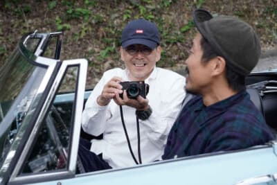 ダットサン1500 スポーツロードスター：長くヒストリックカー趣味を楽しむ弘章さん。ライカを構えて笑顔を見せてくれた。もちろん、カメラにもこだわりがある