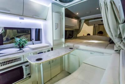 トヨタ ハイエース：サイドのスライドドアから車内に入ると、大きな家庭用冷蔵庫、電子レンジ、IHヒーターなどの家電製品を設置した家具が目を引く