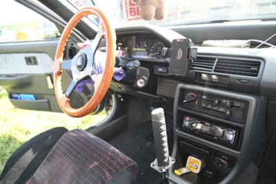 昭和なカスタムの代表的パターンのウッドステアリングに刀シフトレバー。スマホホルダーはエアコン差し込み