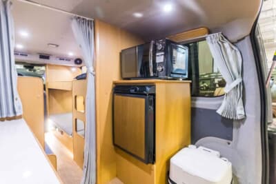 日産 キャラバン:ベッドの後ろに冷蔵庫や電子レンジなどを備えた棚がある