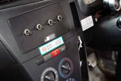 ダイハツ ミラ:センターコンソールに電動ファンのスイッチなどが並ぶ。下のステッカーはレンタカー用か?