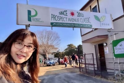 プロスペクトアベニュークラシック: 2012年から続くクラシックカーイベントのゲート前で自撮りをする吉田由美。緑豊かなロケーションに往年の名車が集う、ゆったりとした大人の休日を思わせる空間だ