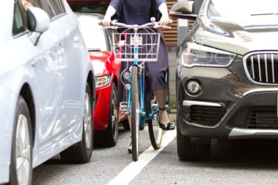 路上駐車の横をすり抜ける自転車。車道の左側を通行できない「やむを得ない場合」に該当するため歩道を通行できるが、ドアの突然の開放（ドアパンチ）など、思わぬ危険が潜む場所でもある