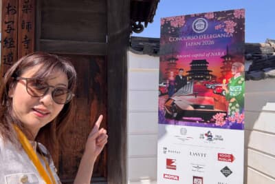 薬師寺入口に設置されたコンコルソ デレガンツァ ジャパン 2026のメインビジュアル看板の前で吉田由美さん。「Ancient capital of NARA」の文字が古都・奈良での開催を印象づける