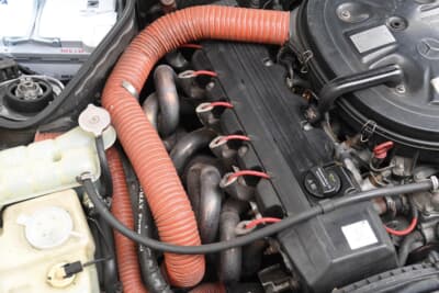 メルセデス・ベンツ 190E：エンジン上部のインテークパイプ。メルセデス純正は前方からのみだが、後方に新たな空気取り込みパイプをAMGが追加。オレンジのパイプは市販の汎用品へと交換されているのだ