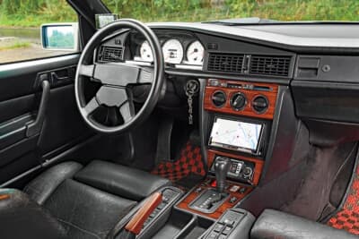メルセデス・ベンツ 190E：ウッドパネルがふんだんにあしらわれた当時の高級感あふれるインテリア。現代のナビゲーションシステムをスマートにインストールし、日常的な使い勝手も大幅に向上させている