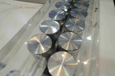 水が充填されたフレキシブルフォイルクーラーが円筒形セルの側面に密着した状態。透明ケースで内部を可視化した展示品で、充填前後の形状変化を確認できる