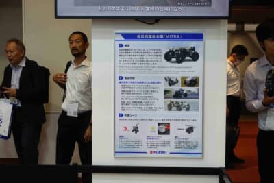 スズキ 多目的電動台車「MITRA」:製品概要・製品特徴・利用シーンを紹介したパネル。前後左右のサスペンションと後輪左右独立モーターを備え、段差や不整地でも安定走行を実現する「ロボットの足」として開発された