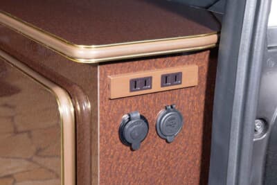 トヨタ ハイエース:キャビネットの側面に配置された家庭用100Vコンセントとシガーソケット。1500Wインバーターの恩恵で、電気ケトルなどの家電も気兼ねなく使用することができる