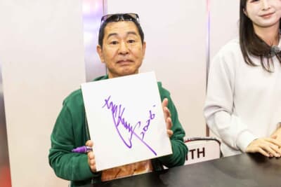 書き上げられた直筆サインを手に笑顔を見せる土屋氏。ビューティフルカーズの技術への信頼があるからこそ実現した、今回の熱いコラボレーションを象徴する一枚だ