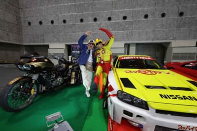 LB-ER34 Super Silhouette SKYLINE：大阪オートメッセ2026のリバティウォークブース。ゴールドのバイクと並ぶのは異色のスッパイマン仕様だ。駄菓子とスーパーカスタムが融合した昭和のヤンチャな世界観にギャラリーは釘付けになった