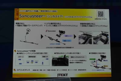 ジェイテクト：Syncusteer™（シンカステア）の特徴を解説するパネル。電動化からリンクレス構造、格納ステアリングコラムまで3段階の進化が示されている