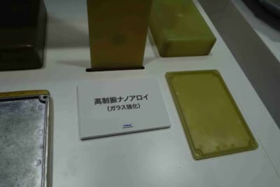 東レブース:高制振ナノアロイ(ガラス強化)の成形品サンプル。アルミ製の既存部品と並べて展示され、代替素材としての可能性を示している