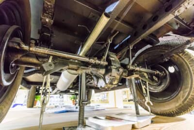 日本内燃機 九五式小型乗用車：展示台の下から望む床下構造。リジッドアクスルと前後を貫くプロペラシャフトが、車軸へ動力を分配する四駆機構を露わにする