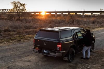 三菱 トライトン:夕暮れの河川敷で車に乗り込むオーナー。キャノピー装着で全長の長いSUVのようなシルエットに変貌した